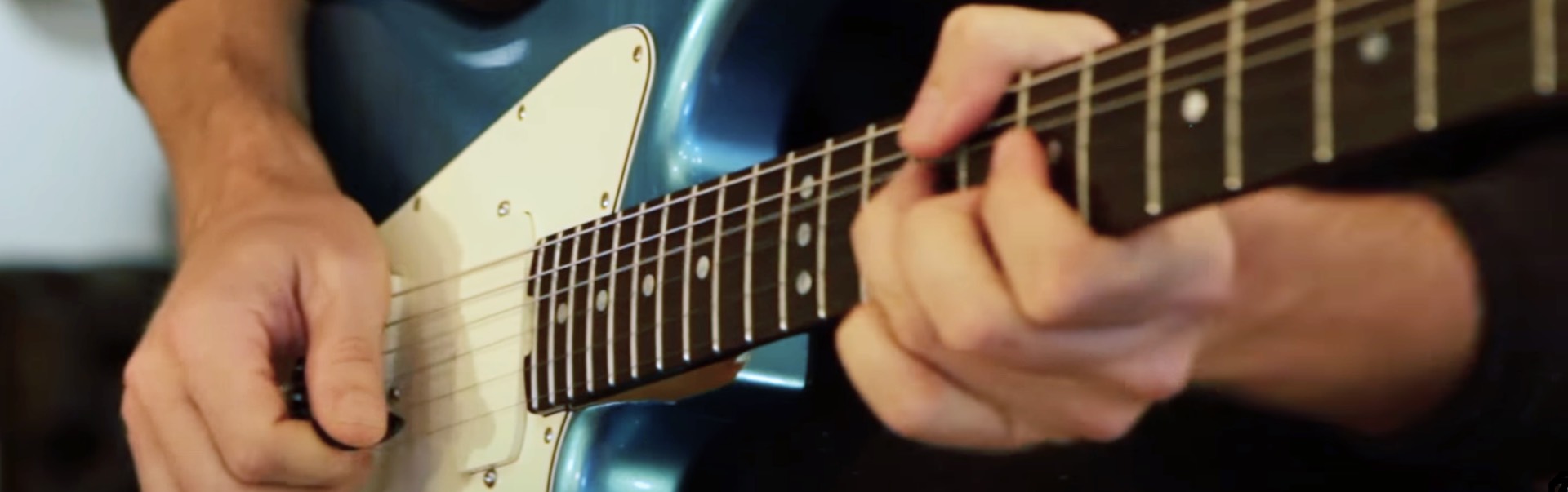 Close up picture of hands playing a turquoise Swope guitar.